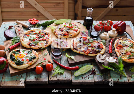 Pizza und Wein Partei. Pizza und rohes Gemüse in Hülle und Fülle auf Eiche Schneidebretter über schäbige blau Holz- Hintergrund horizontal Stockfoto