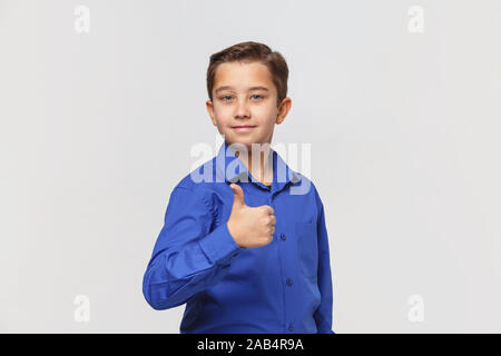 Lächelnde Junge in Blau Classic Shirt zeigt Daumen hoch Stockfoto