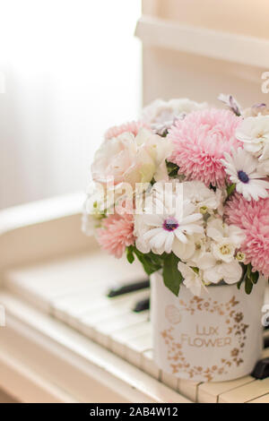 Die Zustellung der Blumen in einer schönen Box auf einem weißen Piano. Blumenstrauß aus Astern, Hortensien und Gänseblümchen. Brautstrauß. Stockfoto