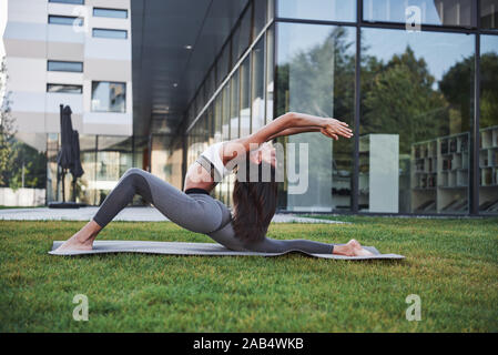 Sonnigen Sommermorgen. Junge athletische Frau macht Handstand auf Stadt Park Street unter den modernen städtischen Gebäuden. Übung im Freien gesunden Lebensstil Stockfoto