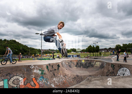 Einer der britischen Top roller Rider Josh Glas üben an der lokalen Skatepark, Stunts auf der ganzen Skatepark mit Menschen beobachten auf Stockfoto