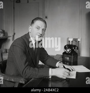 1950, historische, post-WW2 Großbritannien und ein Vorstand eines großen Industriellen Geschäft sitzt an seinem Schreibtisch in seinem Büro einen Brief schreiben, mit einem Telefon der Ära neben ihm, England, UK. Stockfoto