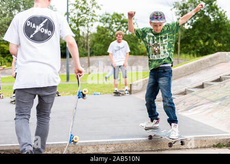 Einen kleinen Jungen mit ADHS, Autismus, Asperger Syndrom üben gehen einige Schritte an der lokalen Skatepark mit seinem Skateboard Instructor aufpassen auf Stockfoto