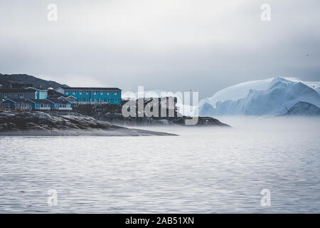 Luftaufnahme der arktischen Stadt Ilulissat, Grönland bei Sonnenaufgang Sonnenuntergang mit Nebel. Bunte Häuser im Zentrum der Stadt mit Eisbergen in der Stockfoto