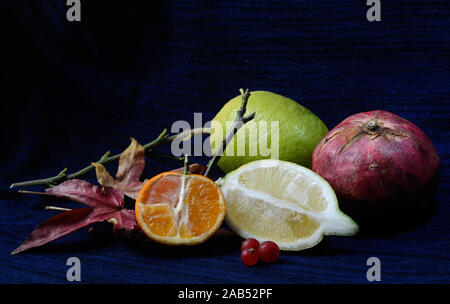 Mandarine und Zitrone und Open-face mit Granatapfel und Ahornblätter gegen einen schwarzen und blauen Hintergrund Stockfoto