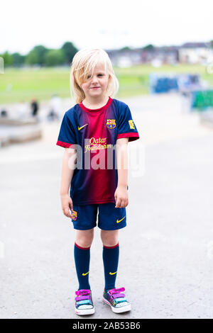 Eine nette, hübsche kleine blonde Mädchen mit einem Football Shirt cheeky, lächelnd und mit viel Spaß im Freien in der britischen Landschaft Stockfoto