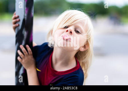 Eine nette, hübsche kleine blonde Mädchen mit einem Football Shirt cheeky, lächelnd und mit viel Spaß im Freien in der britischen Landschaft Stockfoto