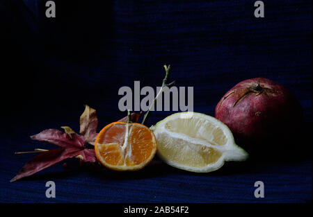 Nahaufnahme von Zitrone und Mandarine mit offenem Gesicht mit einem Granatapfel und Johannisbeeren auf dunkelblauem Hintergrund Stockfoto