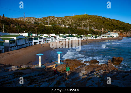 Platja de Les Casetes del Garraf, Garraf, Barcelona, Katalonien. Die markanten kleinen grünen und weißen Strand Häuser sind im Beach Village von Garra Stockfoto