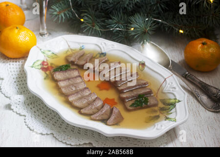 Aspic der Zunge verziert mit gekochten Karotten und Petersilie auf einem festlichen Hintergrund. Rustikaler Stil. Stockfoto