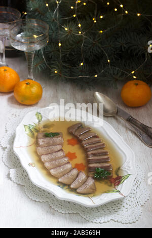 Aspic der Zunge verziert mit gekochten Karotten und Petersilie auf einem festlichen Hintergrund. Rustikaler Stil. Stockfoto