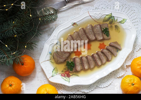Aspic der Zunge verziert mit gekochten Karotten und Petersilie auf einem festlichen Hintergrund. Rustikaler Stil. Stockfoto