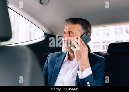 Reifen Geschäftsmann saß auf dem Rücksitz im Auto. Ältere Menschen sprechen über das Handy in ein Taxi. Stockfoto