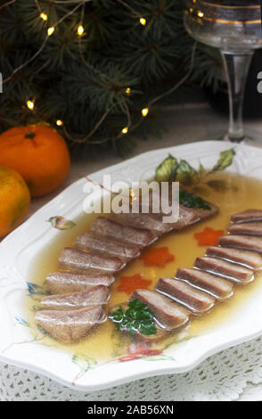 Aspic der Zunge verziert mit gekochten Karotten und Petersilie auf einem festlichen Hintergrund. Rustikaler Stil. Stockfoto