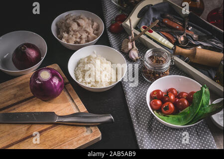 Kochmesser, roten Zwiebeln, Kabeljau Fisch, Fleisch, Reis, Tomaten und Oliven. Zutaten für selbstgemachte Fisch pie. Küche noch Leben Stockfoto