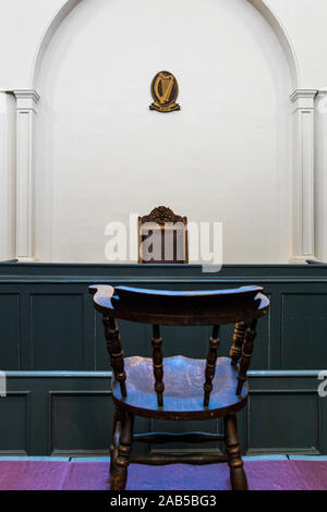 Gerichtssaal in Kilmainham Gaol mit Stuhl am Tisch für die Beklagte und die irische Harfe Symbol an der Wand hinter dem Richter Sitz, Dublin, Irland Stockfoto