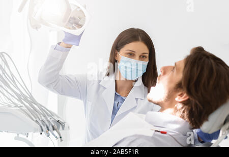 Zahnarzt in Maske Drehen auf die Lampe vor dem Check-up Stockfoto