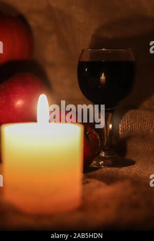 Kerze Flamme Reflexion in einem Glas Rotwein mit rote Äpfel am Sack Hintergrund. Stockfoto