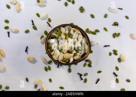 Kokosnuss Schale voller geschälte und ungeschälte Kürbiskerne in weißen Hintergrund mit verstreuten Kürbiskerne und Nelke Gewürz. Stockfoto