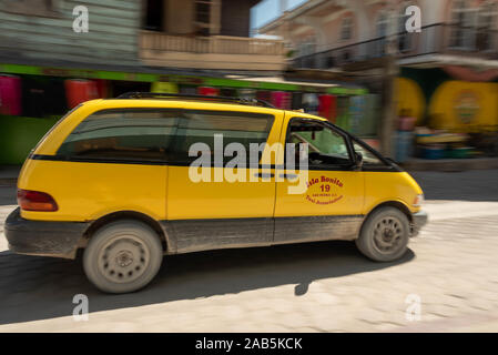 Ein Bild von einem gelben Taxi van Fahren auf der gepflasterten Straße in San Pedro auf Ambergris Caye, Belize. Ein Bild mit einer panning Technik ma genommen Stockfoto