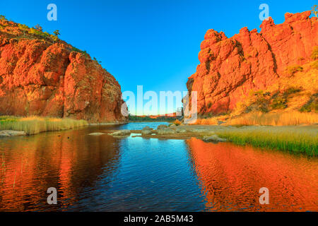 Northern Territory, australische Outback. Malerische Glen Helen Gorge in West MacDonnell Ranges änderungen Farben mit sunrise Licht und reflektiert über wasserloch Stockfoto