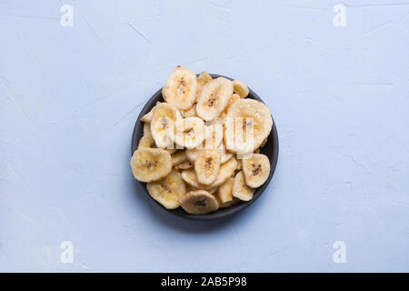 Dehydriert, frische und getrocknete Bananenchips in schwarz Schüssel auf hellen Hintergrund. Blick von oben. Stockfoto