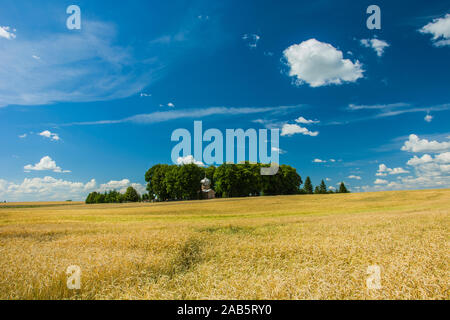 Feld Struktur und eine kleine orthodoxe Kapelle inmitten von Bäumen, weiße Wolken und blauer Himmel - an einem sonnigen Tag Stockfoto