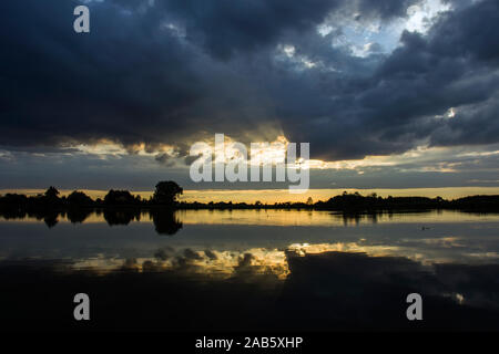 Dunklen regnerischen Wolken und Sonnenstrahlen über das Wasser in die Oberfläche des Sees widerspiegelt - ein Abend anzeigen Stockfoto