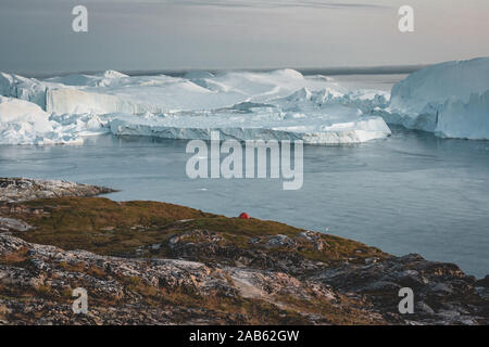 Vening Szene in Ilulissat mit Blick Richtung Kangia Icefjord mit Zelt und schwimmende Eisberge an einem bewölkten Tag Stockfoto