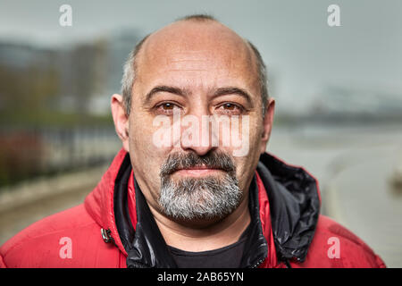 Kahle reife bärtige Mann in roter Jacke steht im Freien. Portrait der alter Mann in warme Kleidung auf der Straße im Herbst. Stockfoto