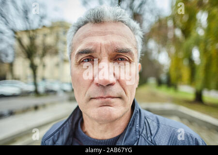 Im Alter von ernsten Mann steht im Freien. Portrait von Reifen traurig Geschäftsmann über 56 Jahre alt auf der Straße. Pension senior Person außerhalb im Herbst. Stockfoto