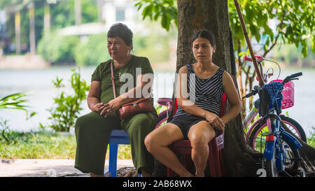 Hanoi, Vietnam - 11. Oktober 2019: Zwei asiatische Frauen im Schatten unter einem Baum sitzen auf Plastikstühlen während einer Hitzewelle in Asien Stockfoto