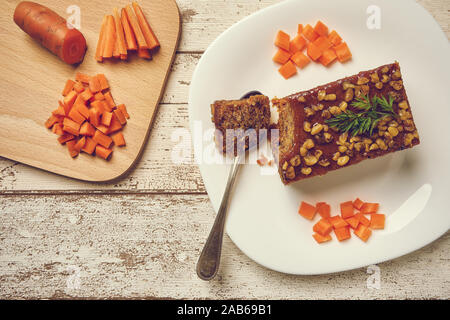 Nachspeise vegane Kuchen mit Kakao, Nussbaum und rohe Karotte. Mit grünen Karotte Blatt dekoriert, weiße Platte und rustikalen Tisch aus alten Brettern. Stockfoto