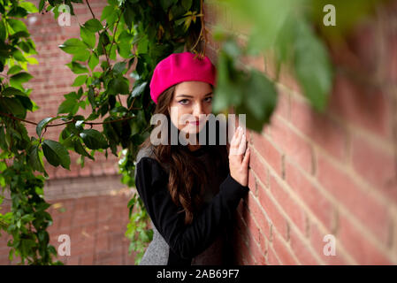 Ein Mädchen in einem rosa Beret steht in der Nähe einer Wand. Stockfoto