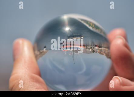 Die Hand hält eine Glaskugel mit Reflexion auf das Meer kosten Stadt Symi und Boote in Griechenland Stockfoto