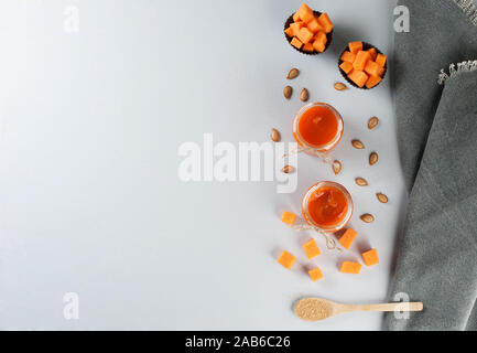 Frische Kürbis Marmelade in Gläser auf dem grauen Hintergrund dekoriert mit Kürbiskernen und braunem Zucker. Herbst Rezepte aus einem Kürbis. Gesunde Ernährung Konzept Stockfoto