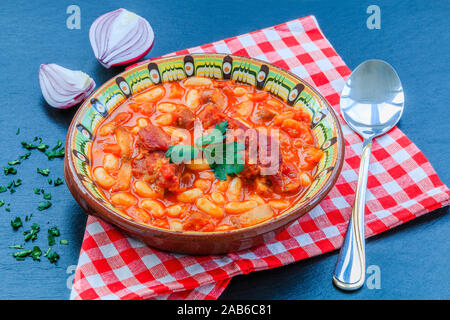 Bohnen Eintopf mit Fleisch und Tomatensoße auf schwarzen Hintergrund mit roten Zwiebeln. Stockfoto