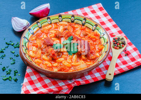 Bohnen Eintopf mit Fleisch und Tomatensoße auf schwarzen Hintergrund mit roten Zwiebeln. Stockfoto