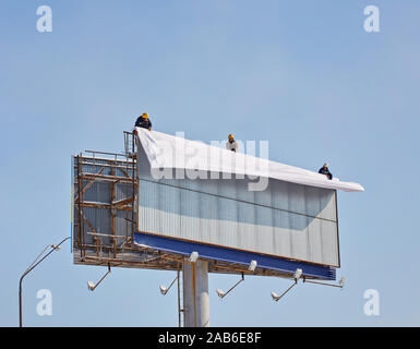 Arbeiter bereitet Billboard zum Einbau neuer Werbung. Industriekletterer arbeiten auf einer Leiter - die Platzierung eines Werbebanners. Stockfoto