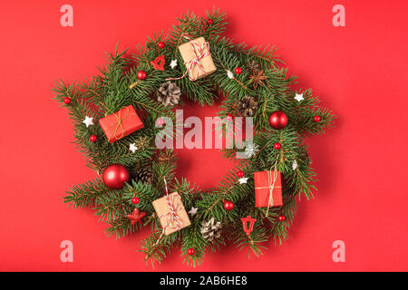 Weihnachten Kranz aus Zweigen Tanne, rot Dekorationen, Geschenkboxen, Tannenzapfen auf rotem Hintergrund. Weihnachten, Winter, neues Jahr. Flach. Stockfoto