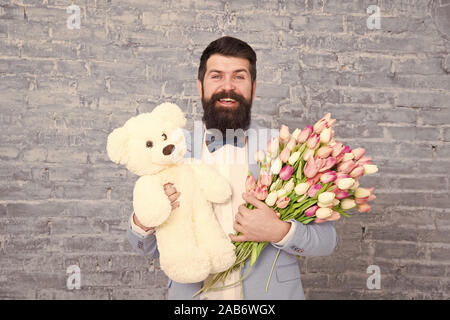 Romantischen Mann. Macho fertig, romantisches Date. Warten auf Darling. Mann gut gepflegt Verschleiß tuxedo Bow Tie halten Blumen Tulpen Bouquet und großen Teddybären Spielzeug. Laden Sie dating. Romantisches Geschenk. Stockfoto