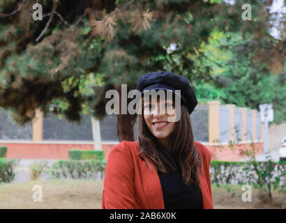 Schöne junge Frau mit roter Jacke und schwarzen Kappe, genießen im Park Stockfoto