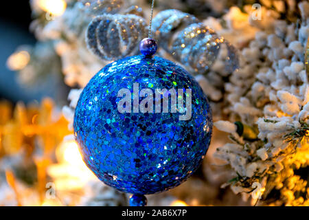 Blau Pailletten Christmas Ball hängen von einer beleuchteten, strömten Weihnachtsbaum ist ein einladender Anblick für eine Familie, ist die Heimat für die Feiertage. Stockfoto