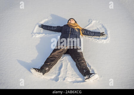 Frau warm gekleidet in einem kalten Winter Wald macht Schnee Engel Abbildung im Park. Kopieren Raum Text Stockfoto