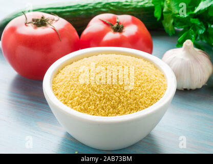 Marokkanisches Couscous in Schüssel, blau Holz- Hintergrund, rustikaler Stil, selektiver Fokus, Seitenansicht. Haufen der rohen Couscous und Gemüse. Stockfoto