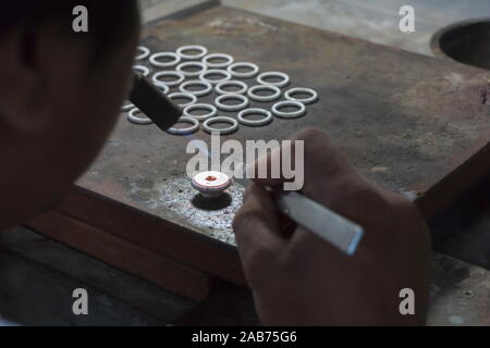 Nahaufnahme eines Männer Goldschmied arbeitet und die Gestaltung eines unfertigen Ring mit einem Werkzeug auf der Workbench in der Werkstatt. Stockfoto