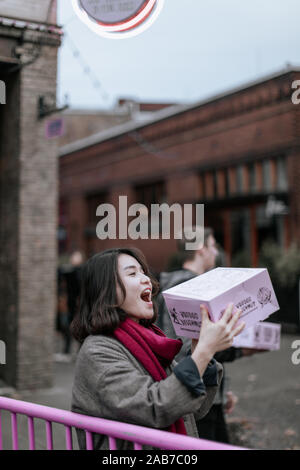 Portland, Oregon - Nov 16, 2019: Asiatische Frauen halten Voodoo donuts Box in der Innenstadt von Portland Stockfoto