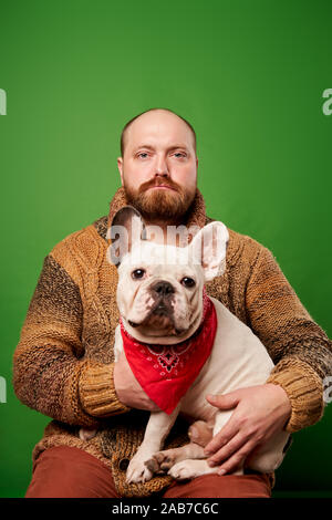 Mann mit Bart mit Französische Bulldogge in seine Arme auf leeren grünen Hintergrund Stockfoto