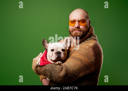 Mann mit Bart mit Ingwer französische Bulldogge in seine Arme auf leeren grünen Hintergrund Stockfoto