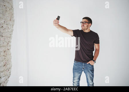 Verspielte bärtiger Mann, der selfie auf Smartphone und weiße Wand im Hintergrund Stockfoto